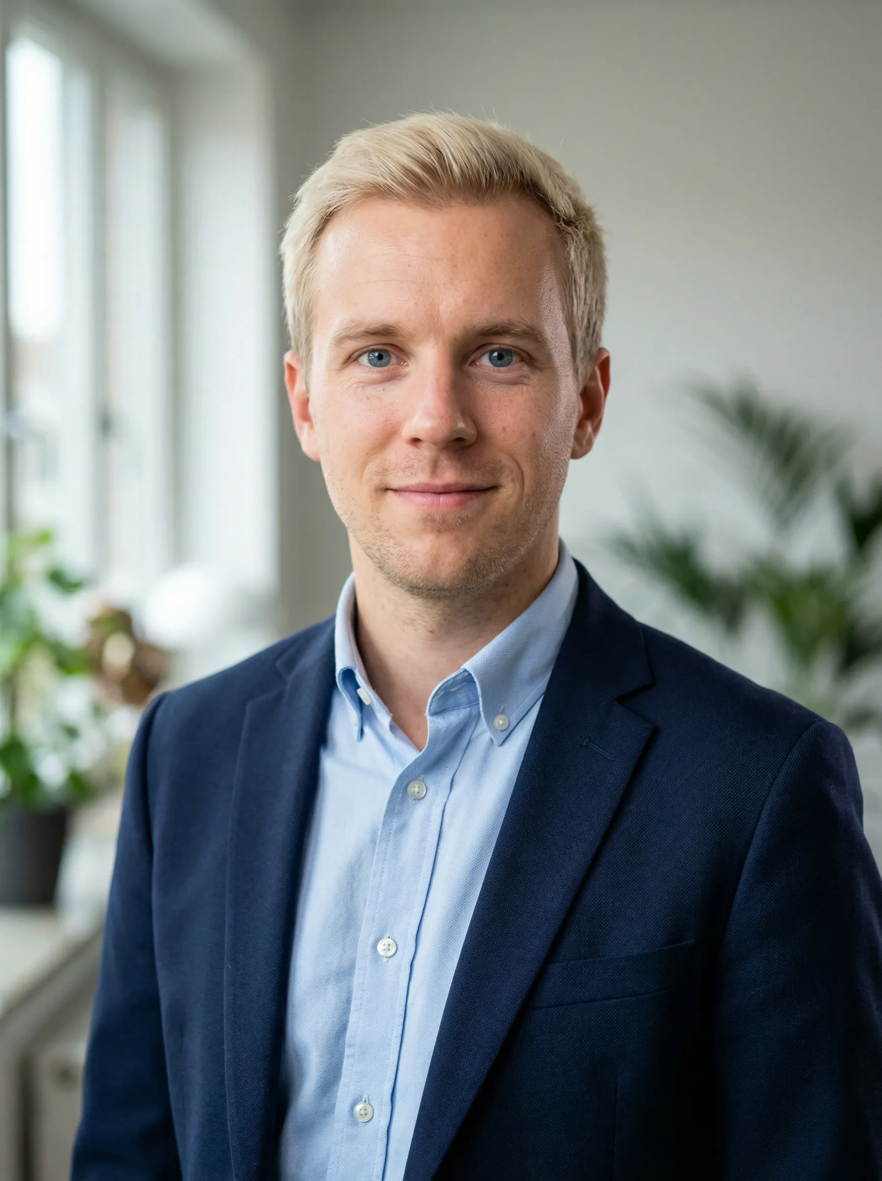 Professional headshot of a man in a navy blazer and light blue shirt in a bright home office